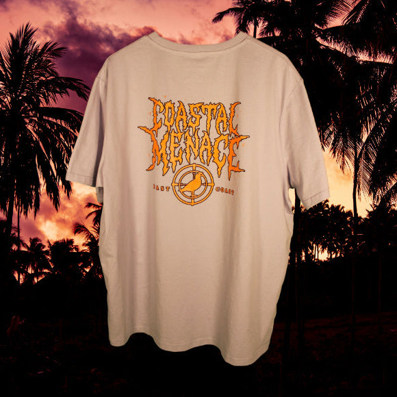 Light purple t-shirt with an orange 'Coastal Menace' graphic design against a palm tree sunset background