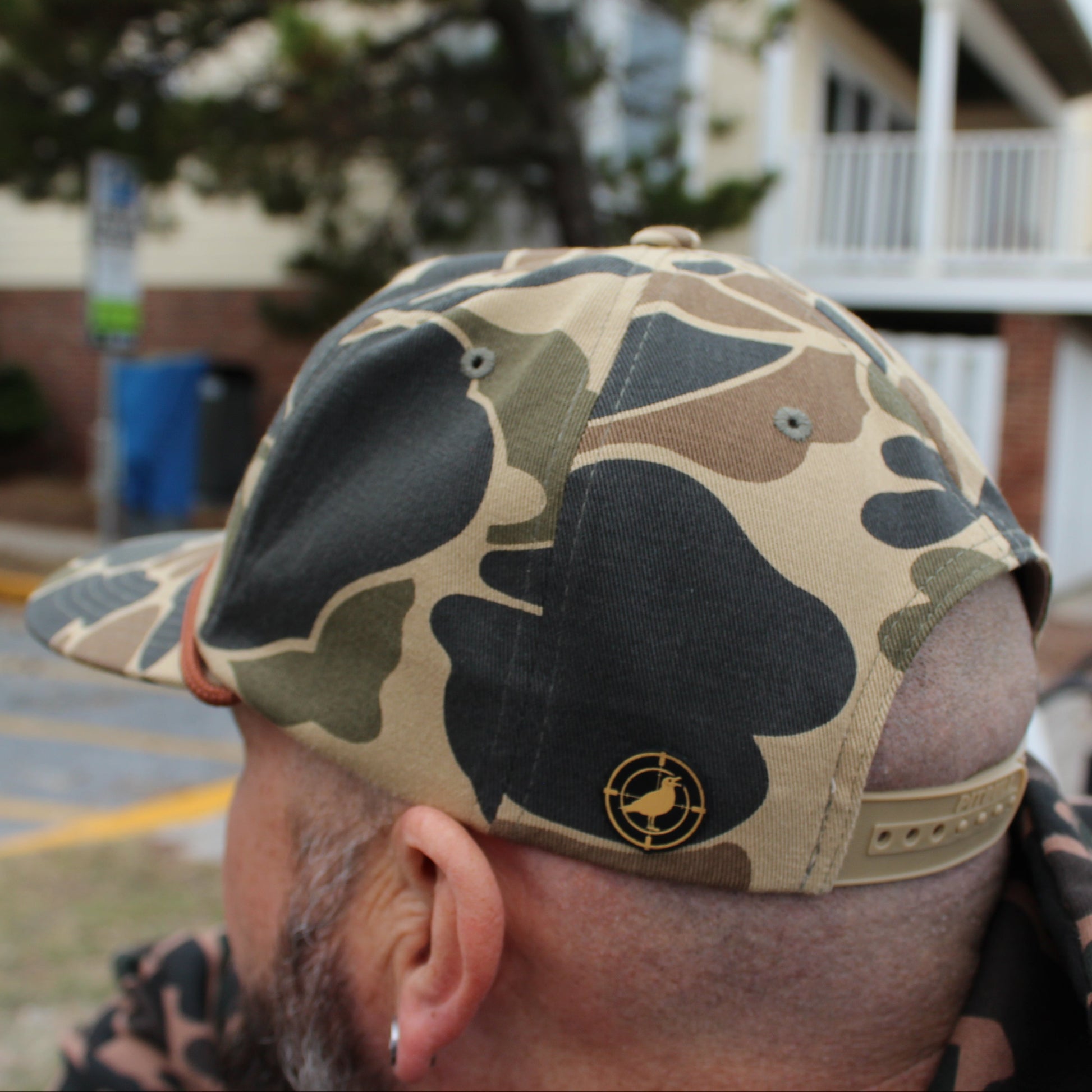 Person wearing a camouflage cap with a seagull logo, standing outdoors.