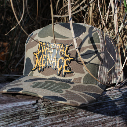 Camouflage cap with "Coastal Menace" patch on a wooden post with beach grass background