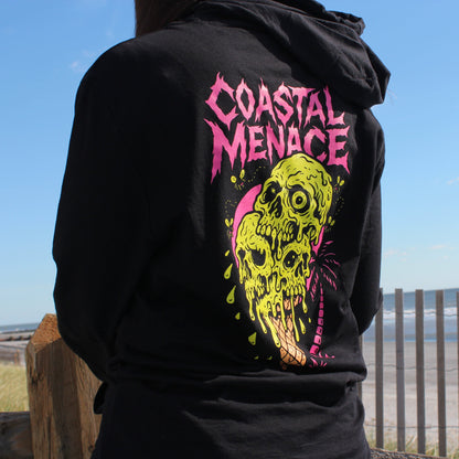 Black hoodie with 'Coastal Menace' design on the back, worn by a person at a beach.