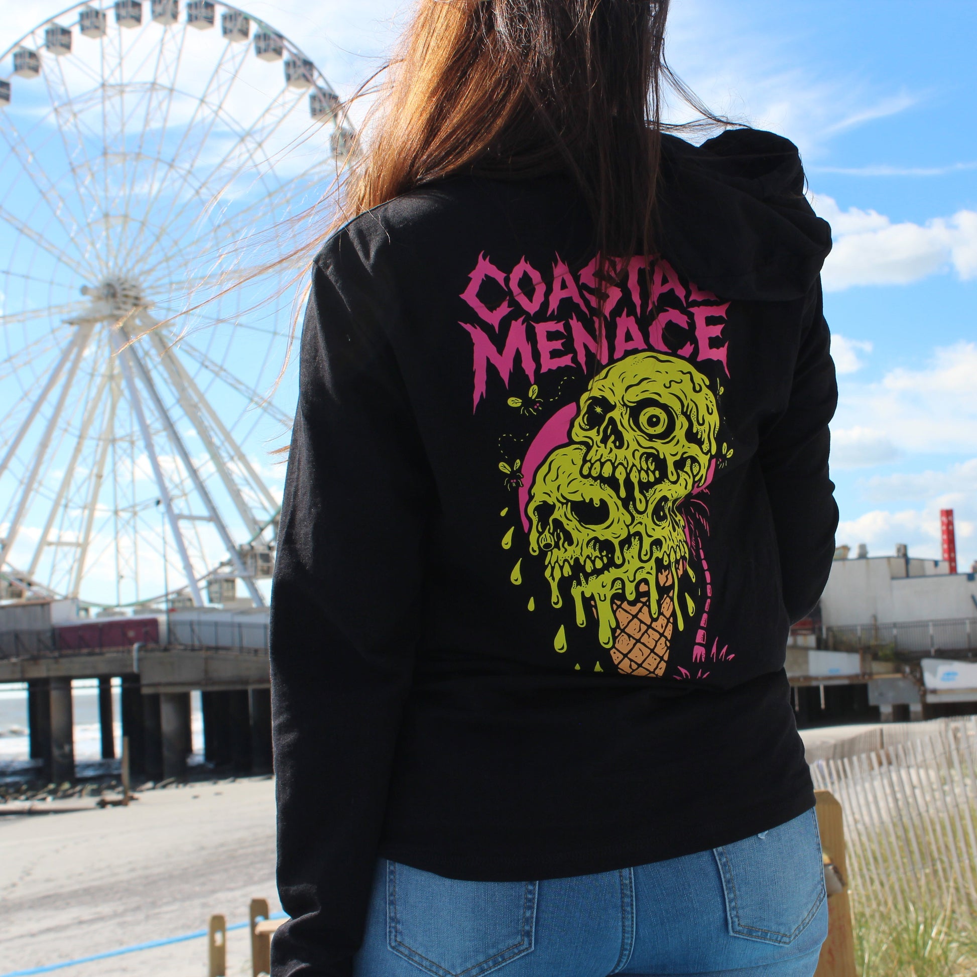 Person wearing a black hoodie with a colorful graphic design in front of a Ferris wheel.