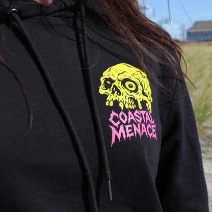 Black hoodie with green and pink skull design on a girl by the beach.