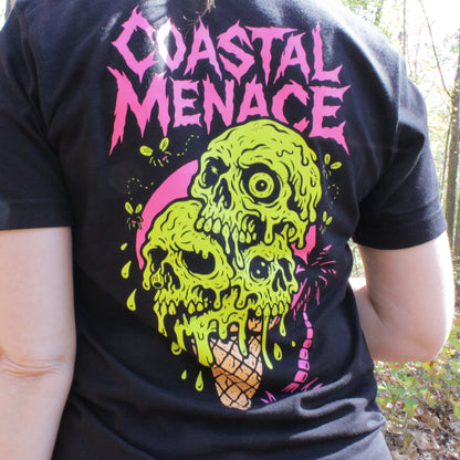 Person wearing a black t-shirt with a colorful skull design and 'Coastal Menace' text in a forest setting.