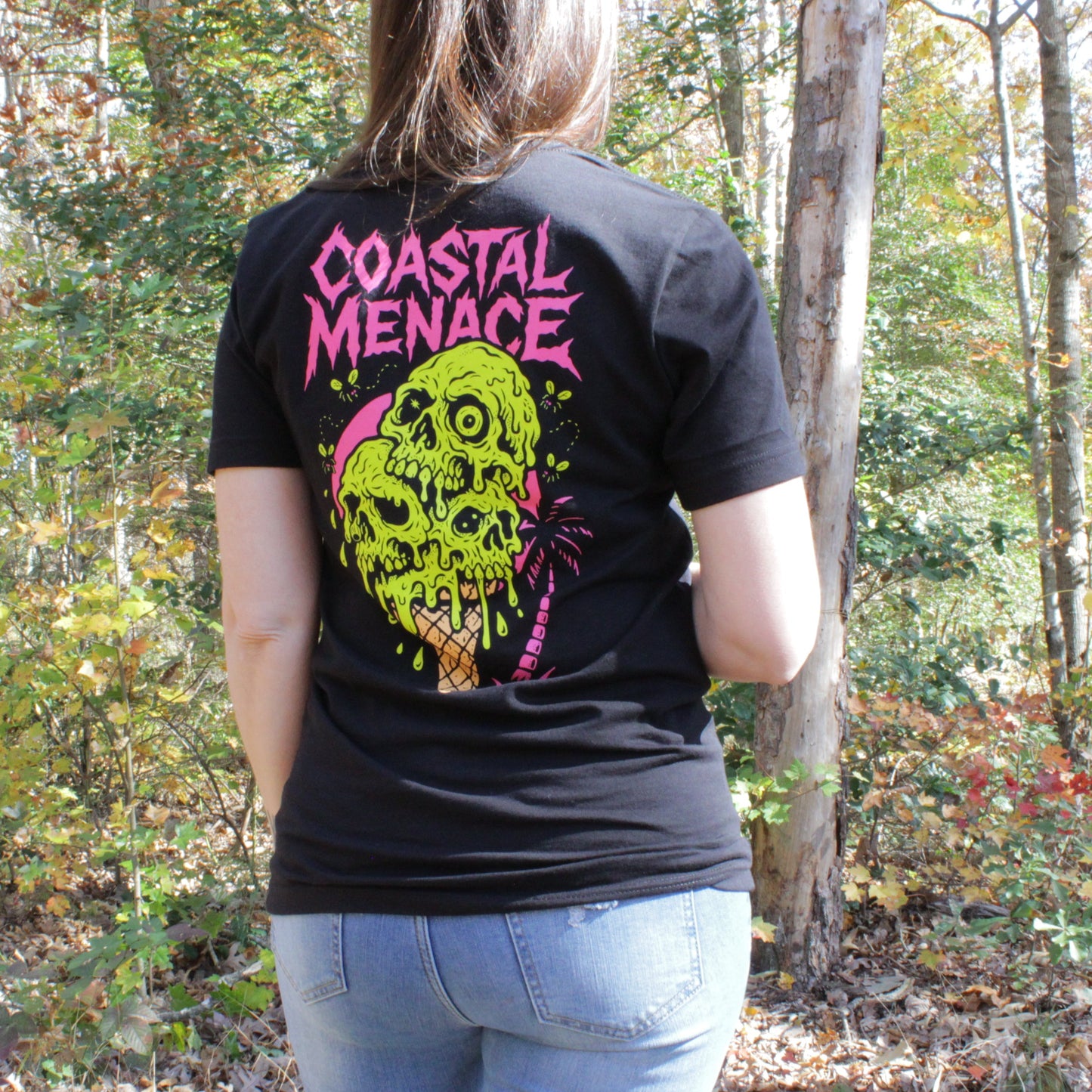 Femal wearing a black t-shirt with 'Coastal Menace' design in a forest setting