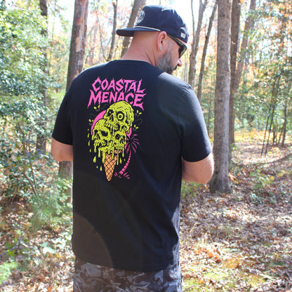 Man wearing a black t-shirt with colorful skull 'Coastal Menace' design in the woods