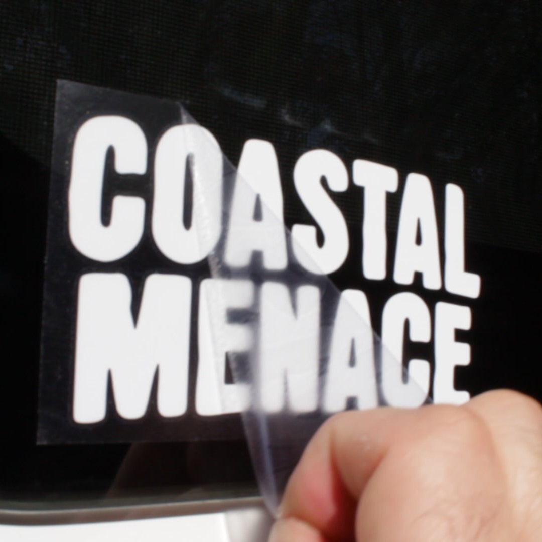 Hand applying a 'Coastal Menace' decal to a black surface.