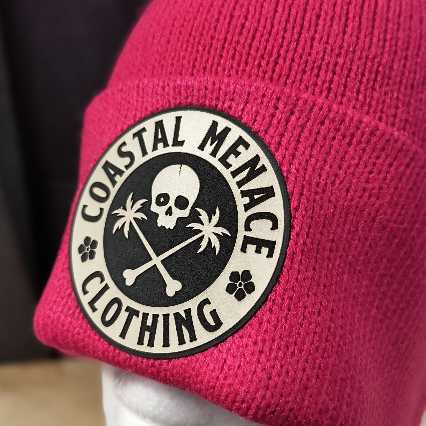 Closeup of raspberry pom beanie and round Coastal Menace patch