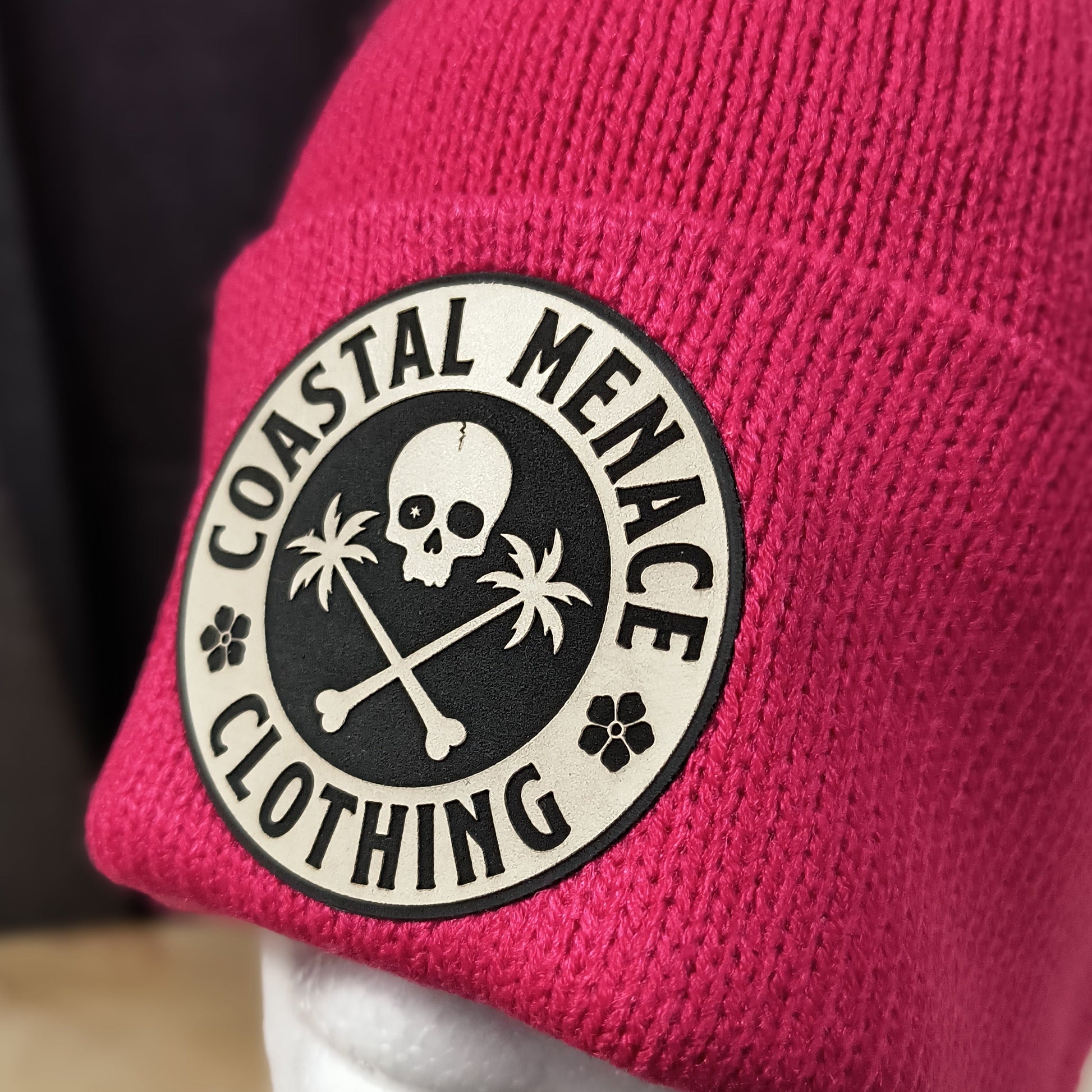 Closeup of raspberry pom beanie and round Coastal Menace patch