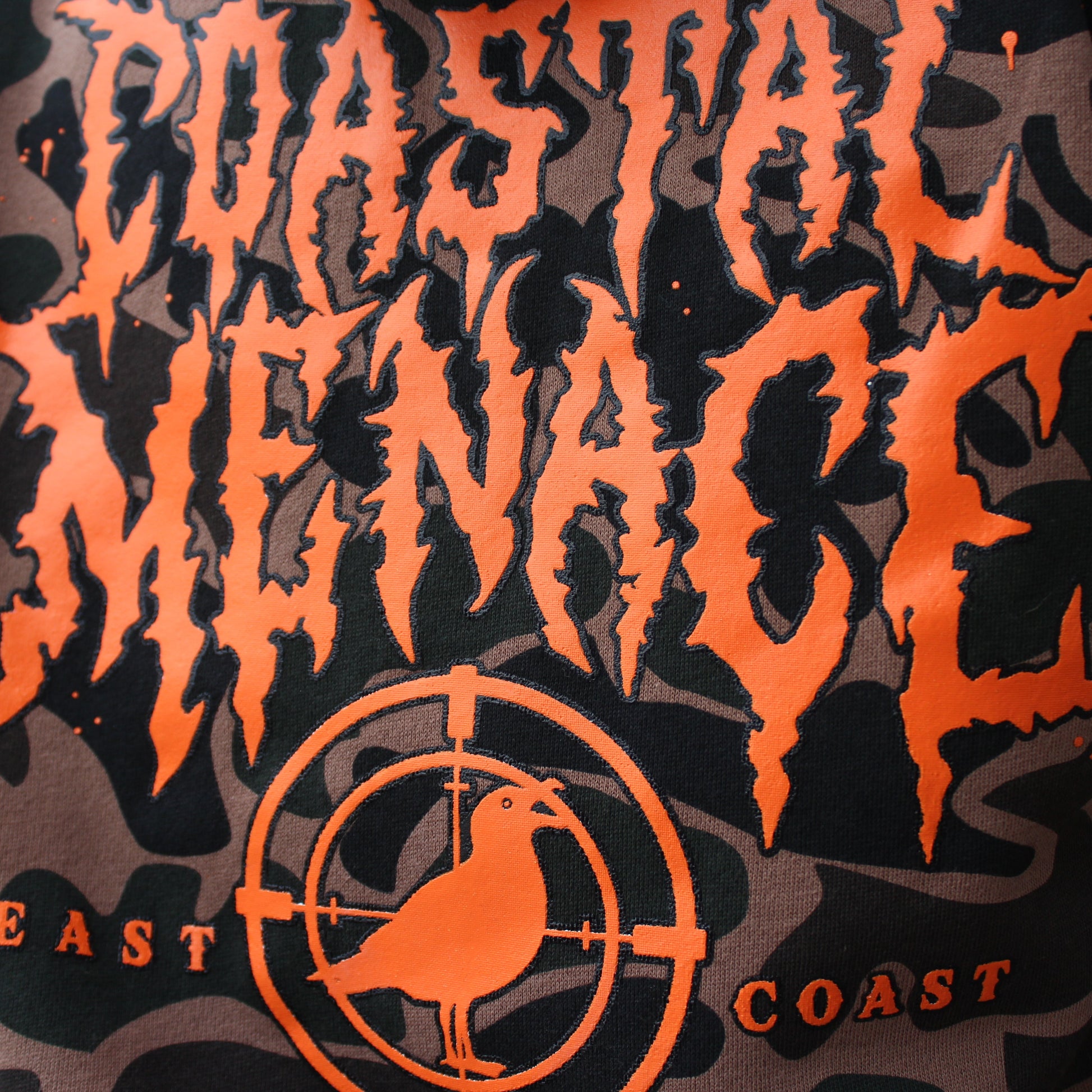 Close-up of a bright orange Coastal Menace printed logo on a camo hoodie.