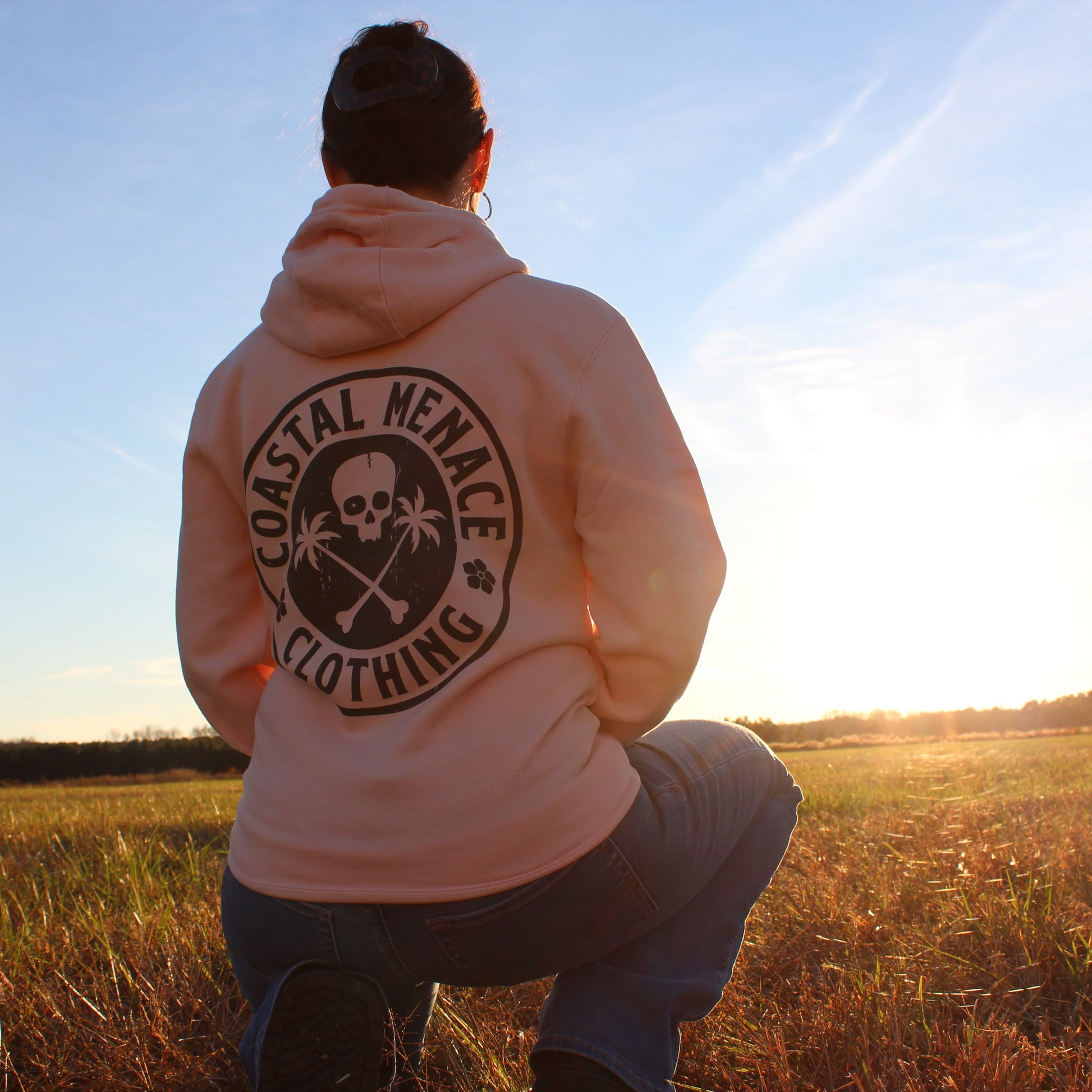 Back view of the Coastal Menace Base Threat pink hoodie, worn outdoors at sunset.