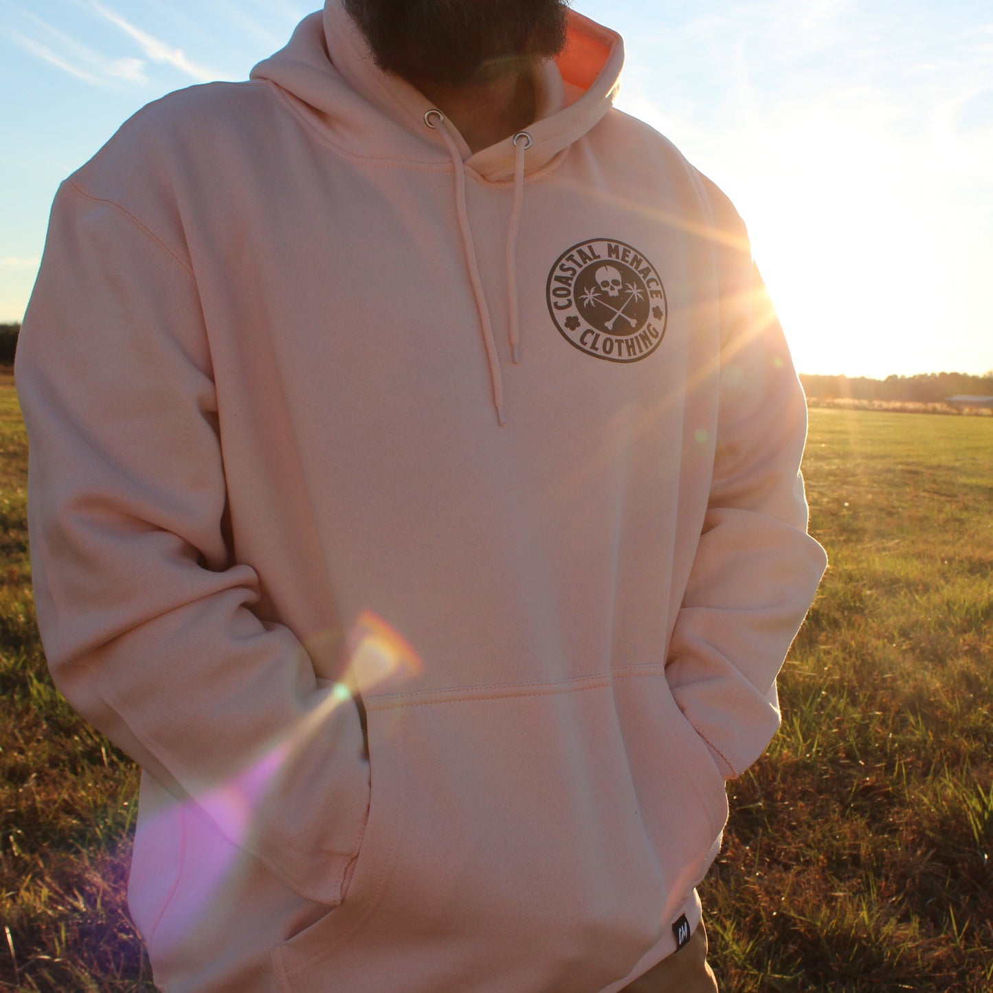 Men’s front view of the Base Threat pink hoodie with sun flare lighting.