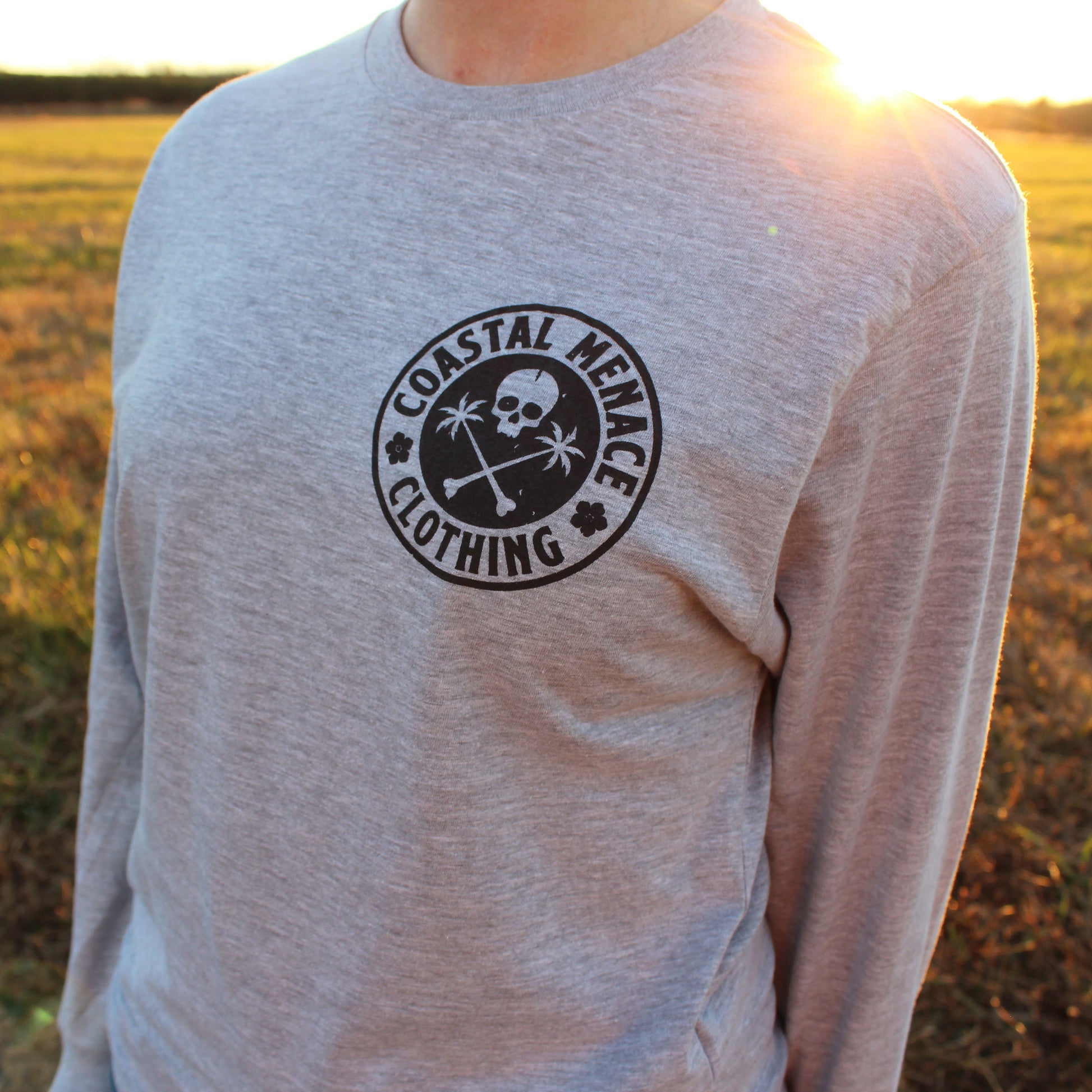 Front view of the Base Threat heather gray long sleeve tee worn outdoors with sun flare lighting.