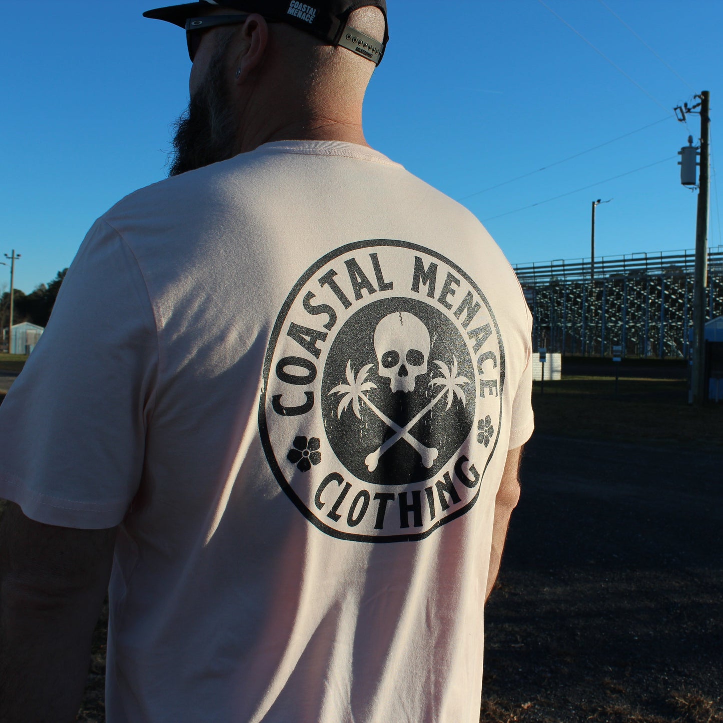 Angled back view of the Coastal Menace Base Threat pink tee worn outdoors.