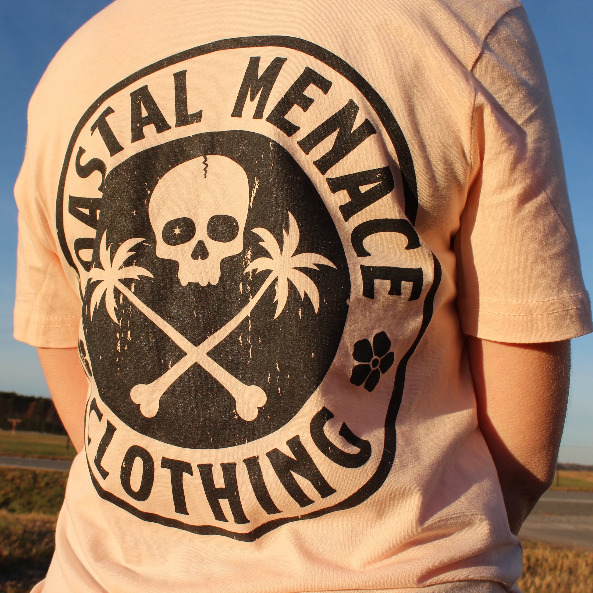 Close-up of the Base Threat pink tee back graphic with skull, crossbones, and palm trees.