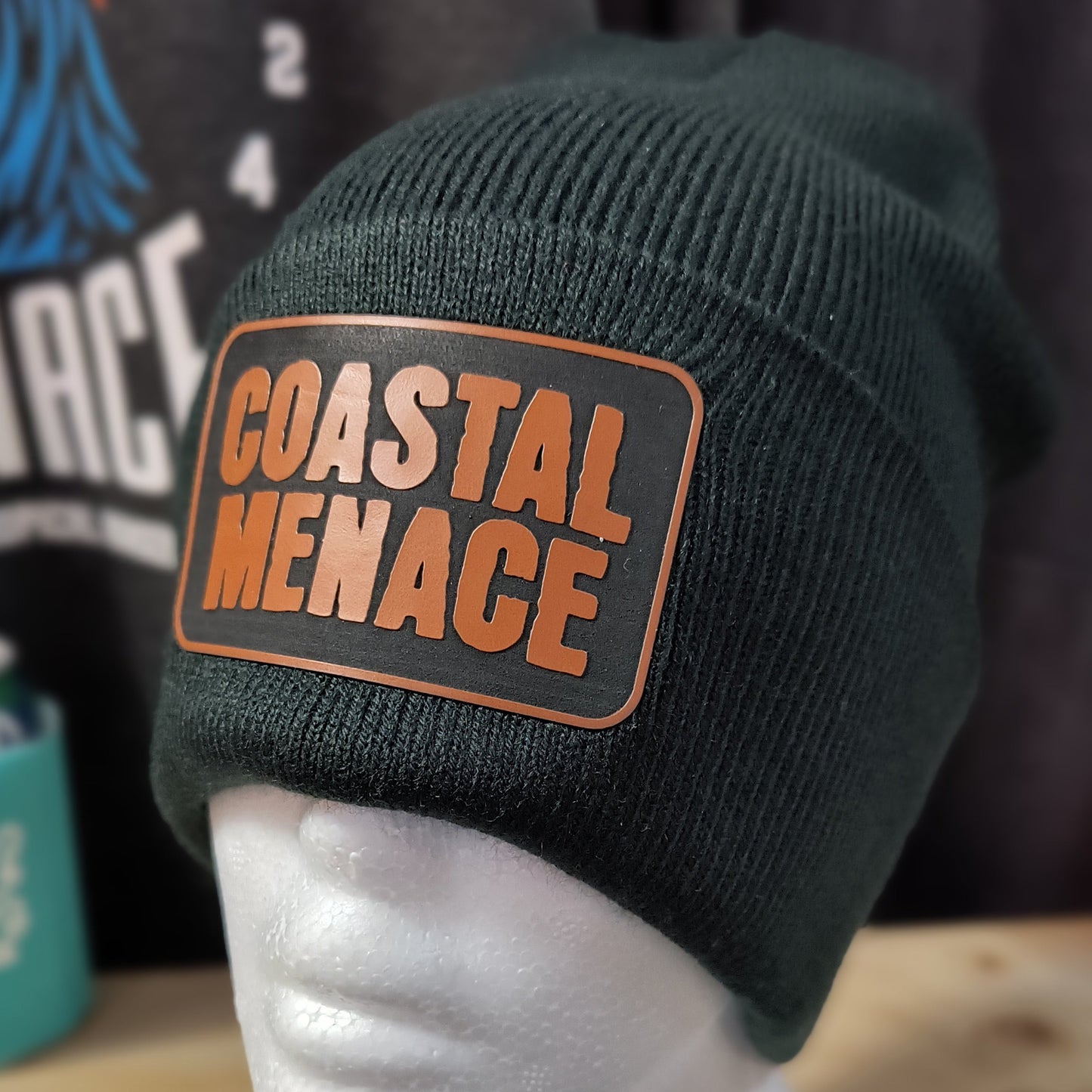 close up of Coastal Menace leather style patch on a black winter beanie