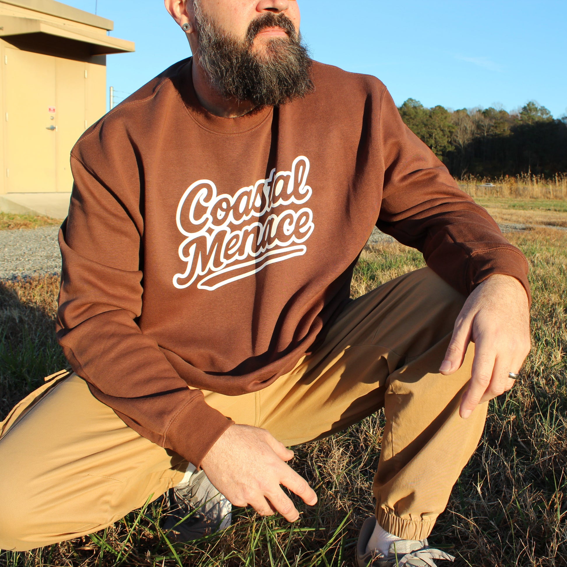 man crouching wearing coastal menace retro script brown crewneck
