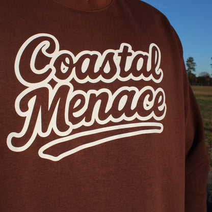 angled close-up of coastal menace retro script logo on brown crewneck