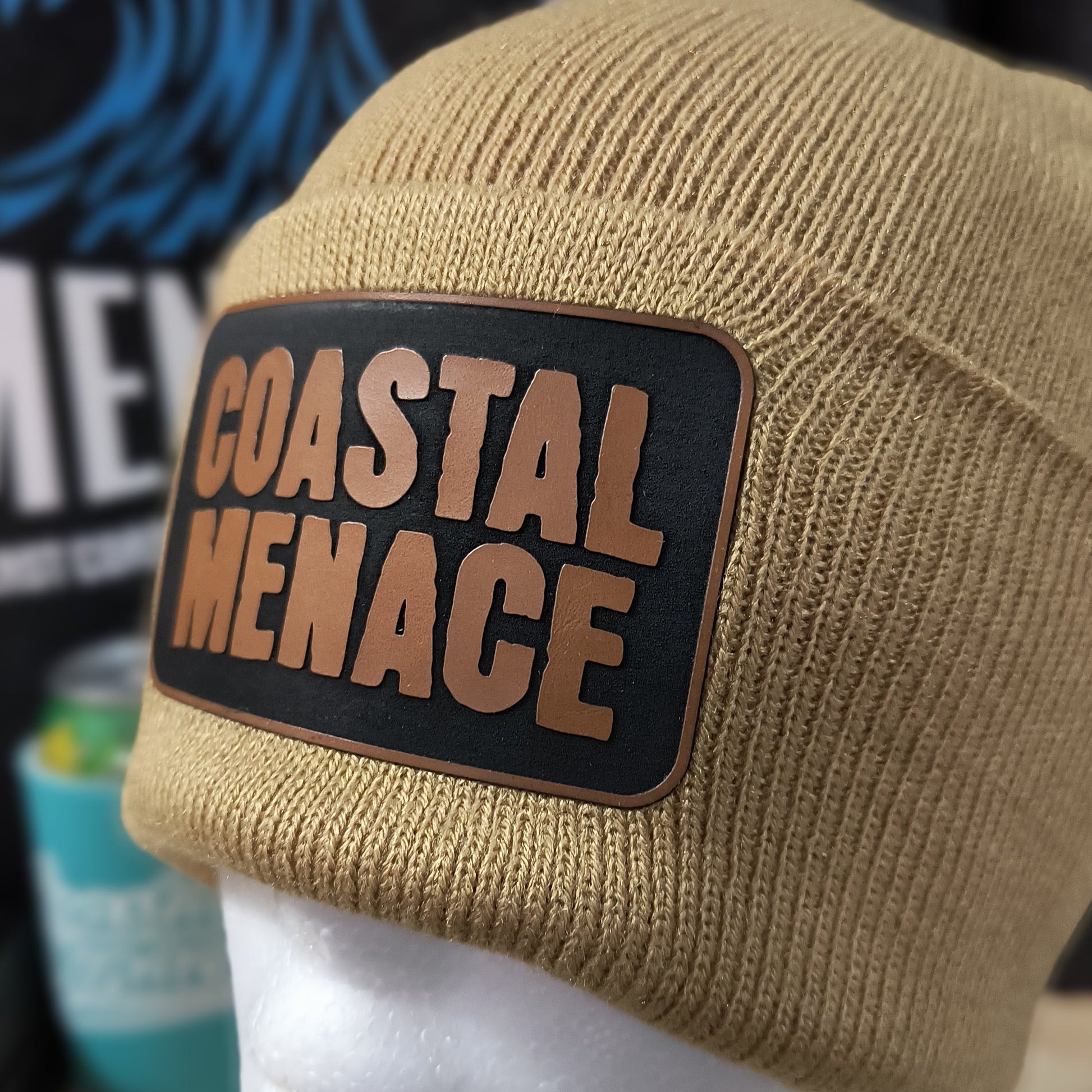 close up of tan Coastal Menace beanie showing leather style logo patch