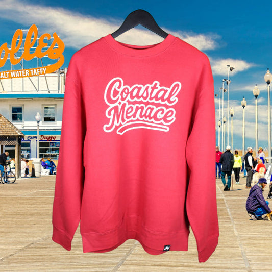 Cardinal red crewneck sweatshirt with large white Coastal Menace retro script logo on the front, displayed on the Rehoboth Beach boardwalk with the Dolles Salt Water Taffy sign in the background