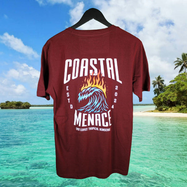 Back view of maroon Coastal Menace Hot Breaker tee featuring large flaming wave graphic and bold lettering, shown in front of a tropical shoreline scene