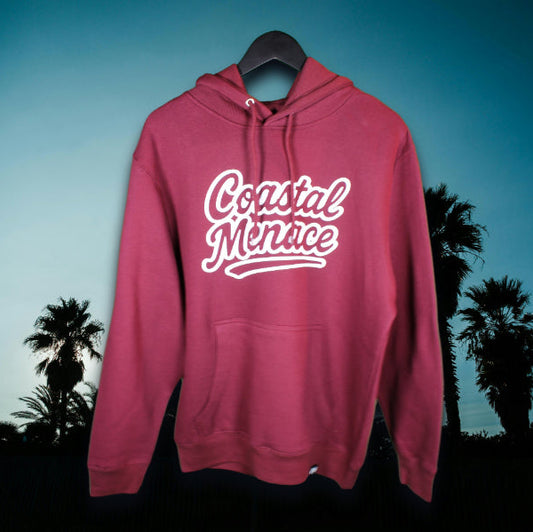 Burgundy-colored hoodie with large white Coastal Menace retro script logo on the front, displayed against a tropical palm-tree sunset backdrop