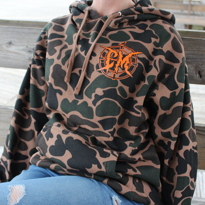 Person wearing a camouflage hoodie with metal style logo sitting on a wooden bench on the boardwalk